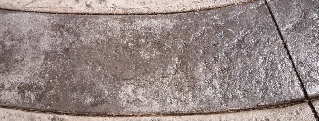 Detalle de un pavimento de hormigón impreso con zonas desgastadas, pérdida de color y manchas blanquecinas irregulares.